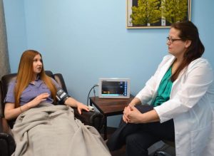 Healthcare provider in white coat consulting with patient wearing blood pressure cuff during appointment in clinical room