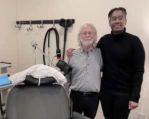 Two clinicians standing beside TMS treatment chair with coil apparatus in clinical treatment room