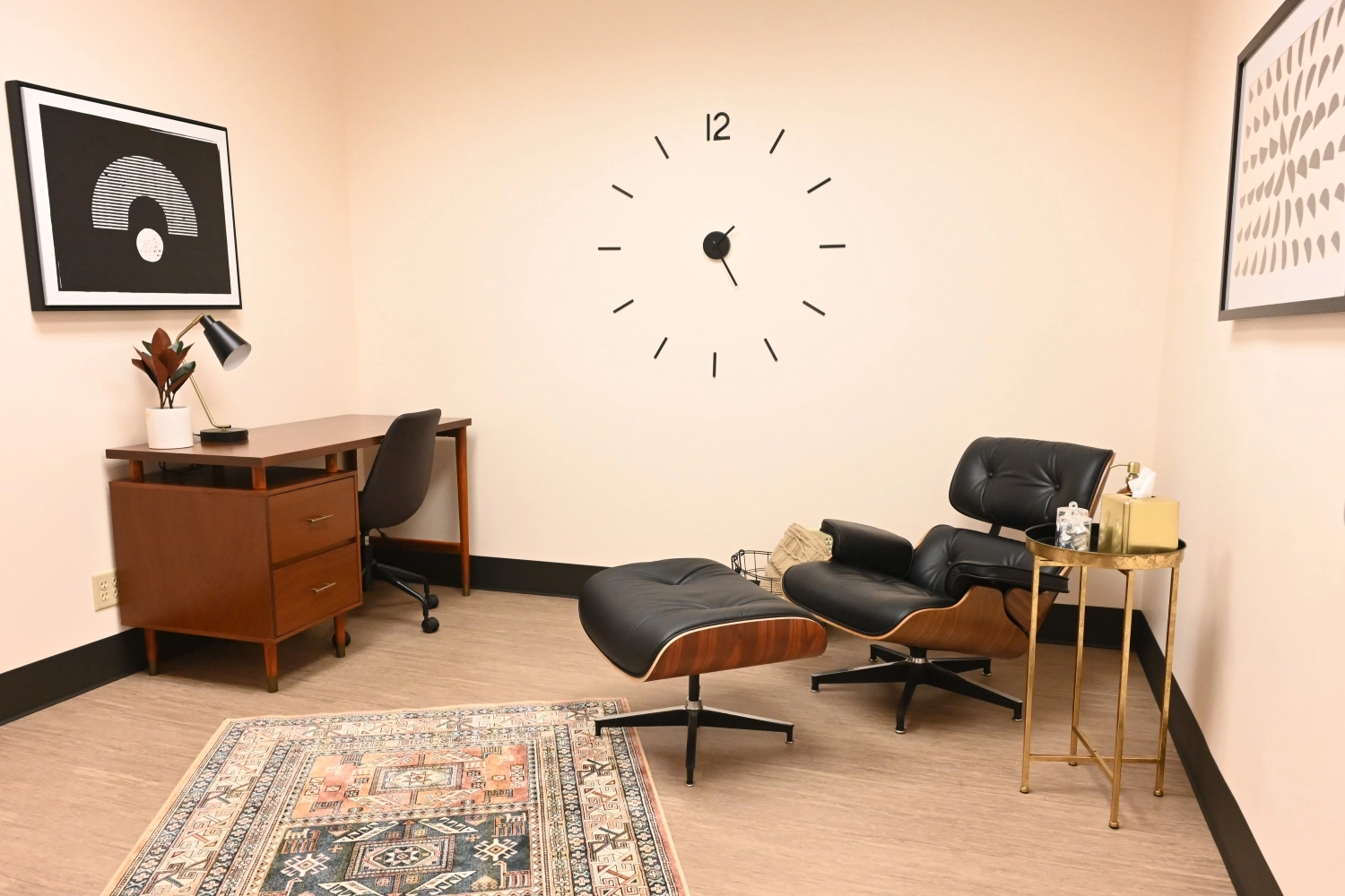 TMS treatment room with black lounge chair, ottoman, wooden desk, and wall clock