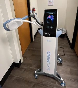 ExoMind TMS device on stand in clinical room with blue treatment coil mounted on articulated arm