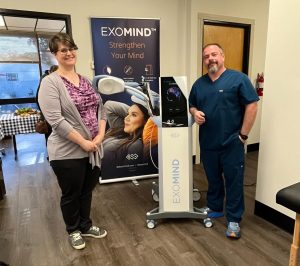 Two healthcare providers standing beside ExoMind TMS device with informational poster in clinical office setting