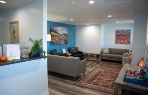 Spacious clinic reception area with blue accent wall, comfortable seating arrangements, artwork, and welcoming front desk