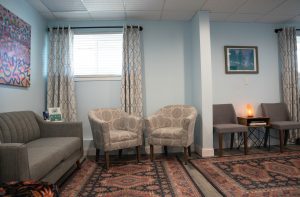 Calm waiting room with gray sofa, patterned armchairs, warm lighting, and artwork on light blue walls
