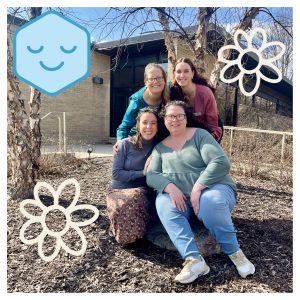 Four smiling staff members posing outdoors by bare tree with white flower decorative elements