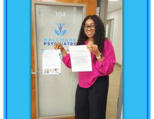 Woman in pink blazer displaying certificates in front of Hallmark Psychiatry office door 304