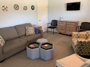 Comfortable waiting lounge with gray sofa, patterned chairs, decorative clocks, hexagon ottomans, and TV mounted on wall