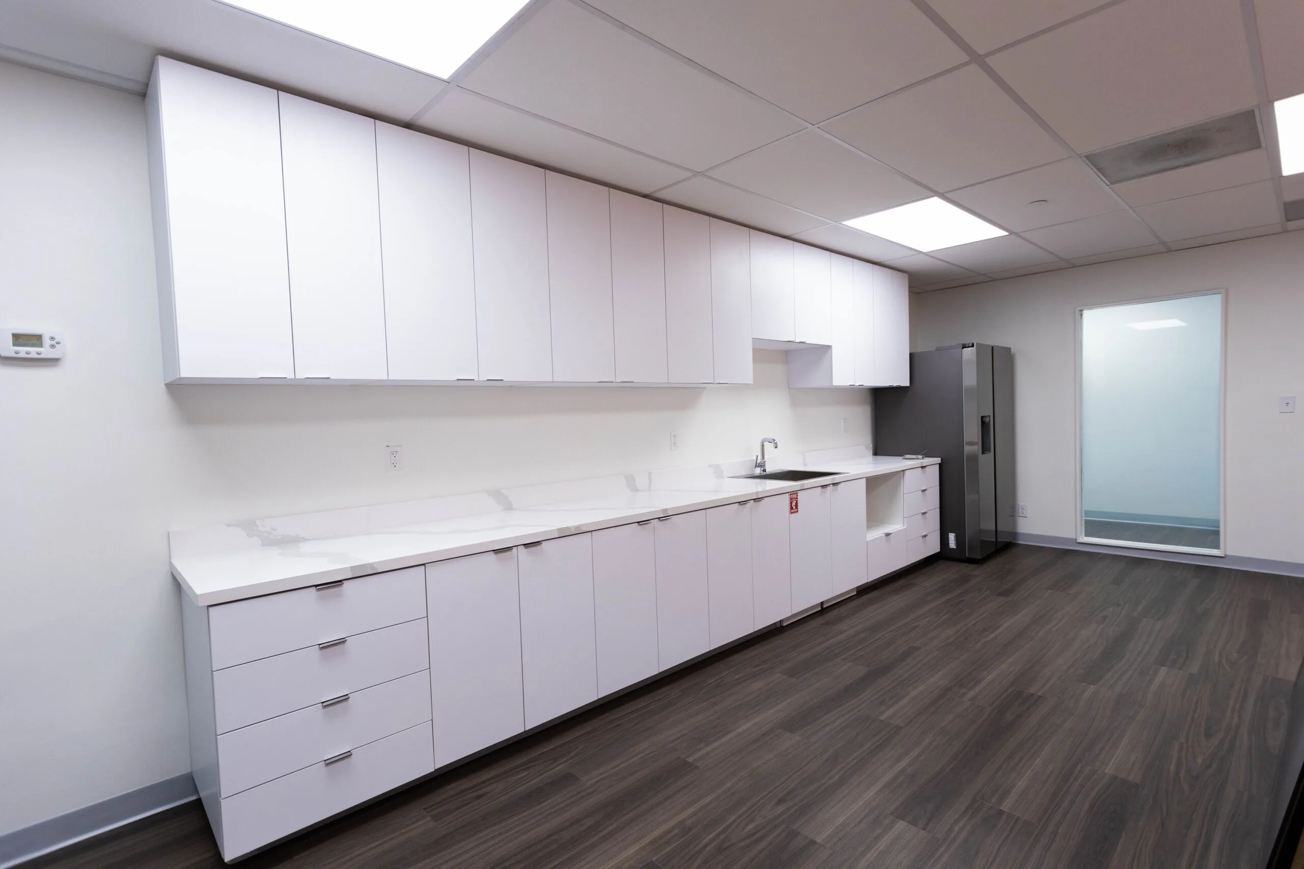 Clinical kitchen area with white cabinetry, stainless steel refrigerator, and dark wood flooring