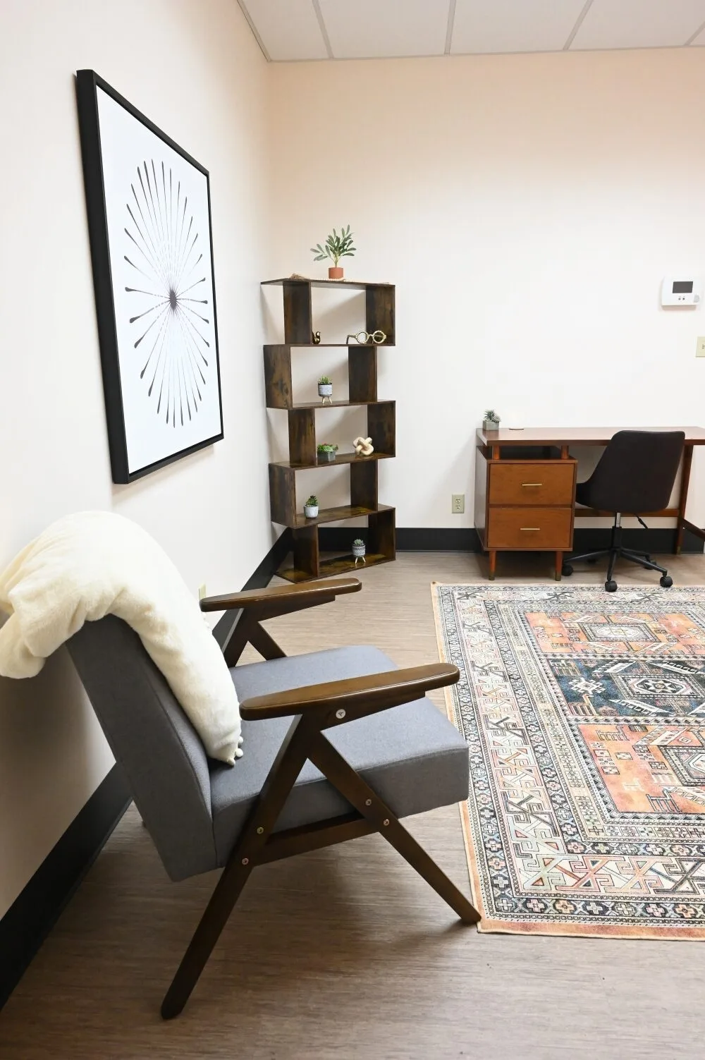 TMS office space with mid-century modern chair, wooden shelving unit, desk, and circular wall art