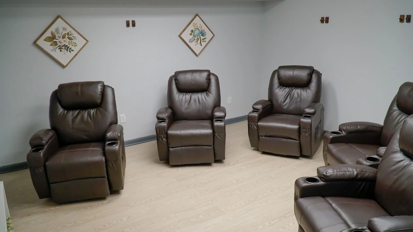 Multiple brown leather recliners arranged in a treatment room with framed botanical artwork on white walls