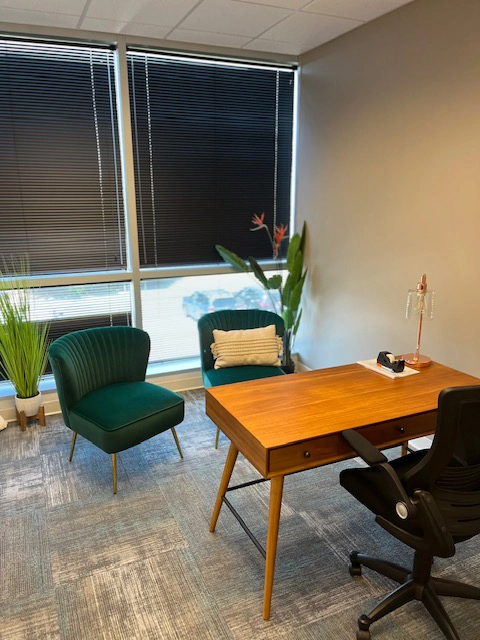 Allen office space with wooden desk, green accent chair, windows, and potted plants