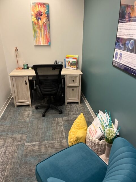 Private office with light wood desk, black office chair, sunflower artwork, educational posters, and decorative elements