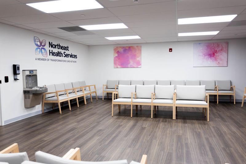 Healthcare waiting room with Northeast Health Services logo, wooden chairs with gray cushions, and pink abstract wall art