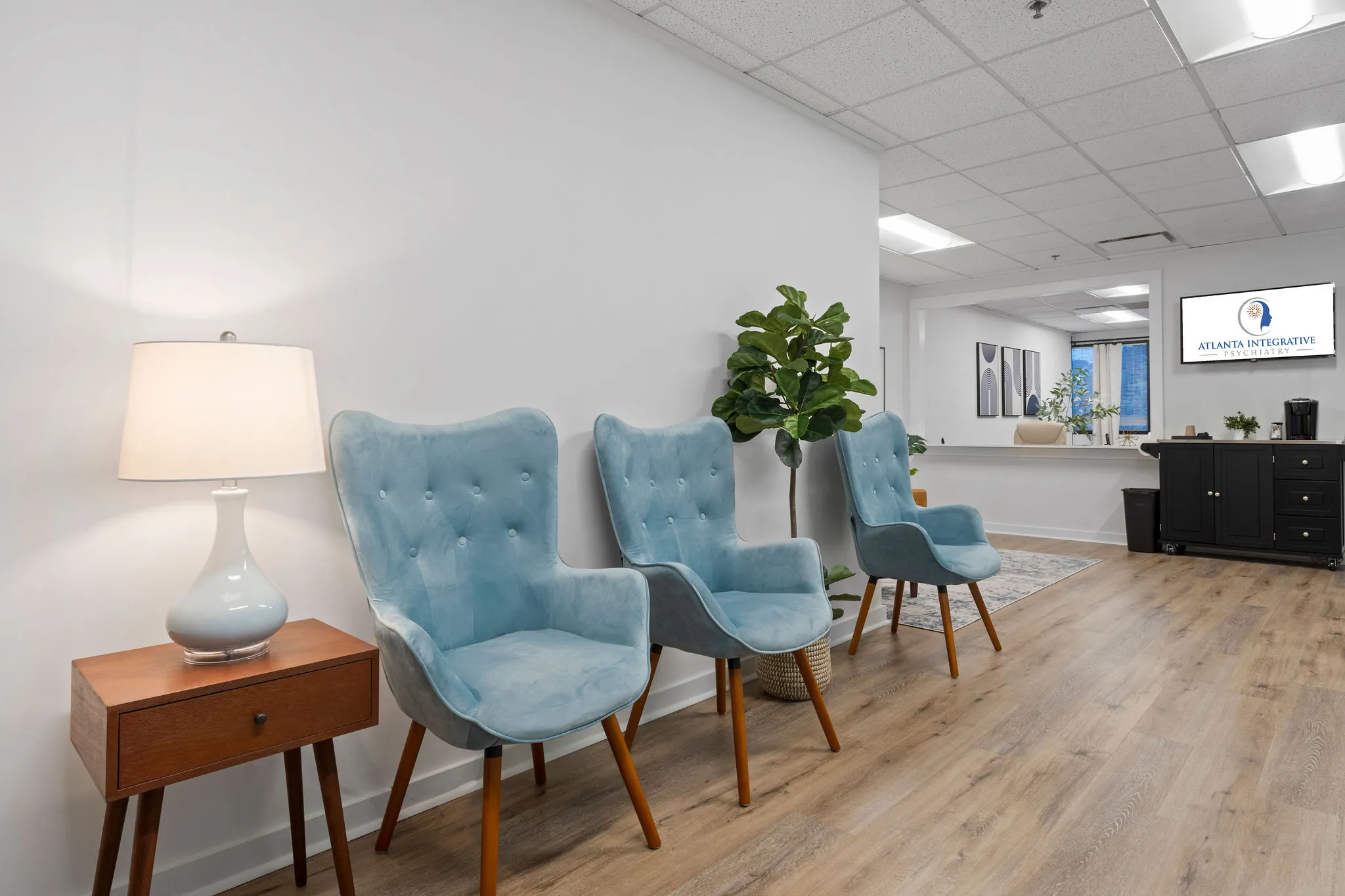 Atlanta Integrative Psychiatry waiting room with light blue chairs, wooden side table, lamp, and reception desk