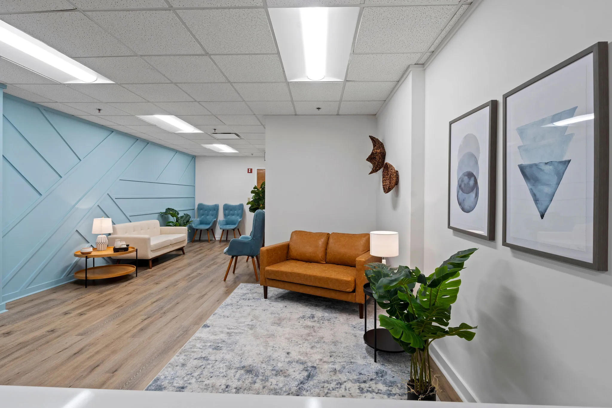 Modern clinic waiting area with tan and blue seating, light blue accent wall, artwork, and potted plant