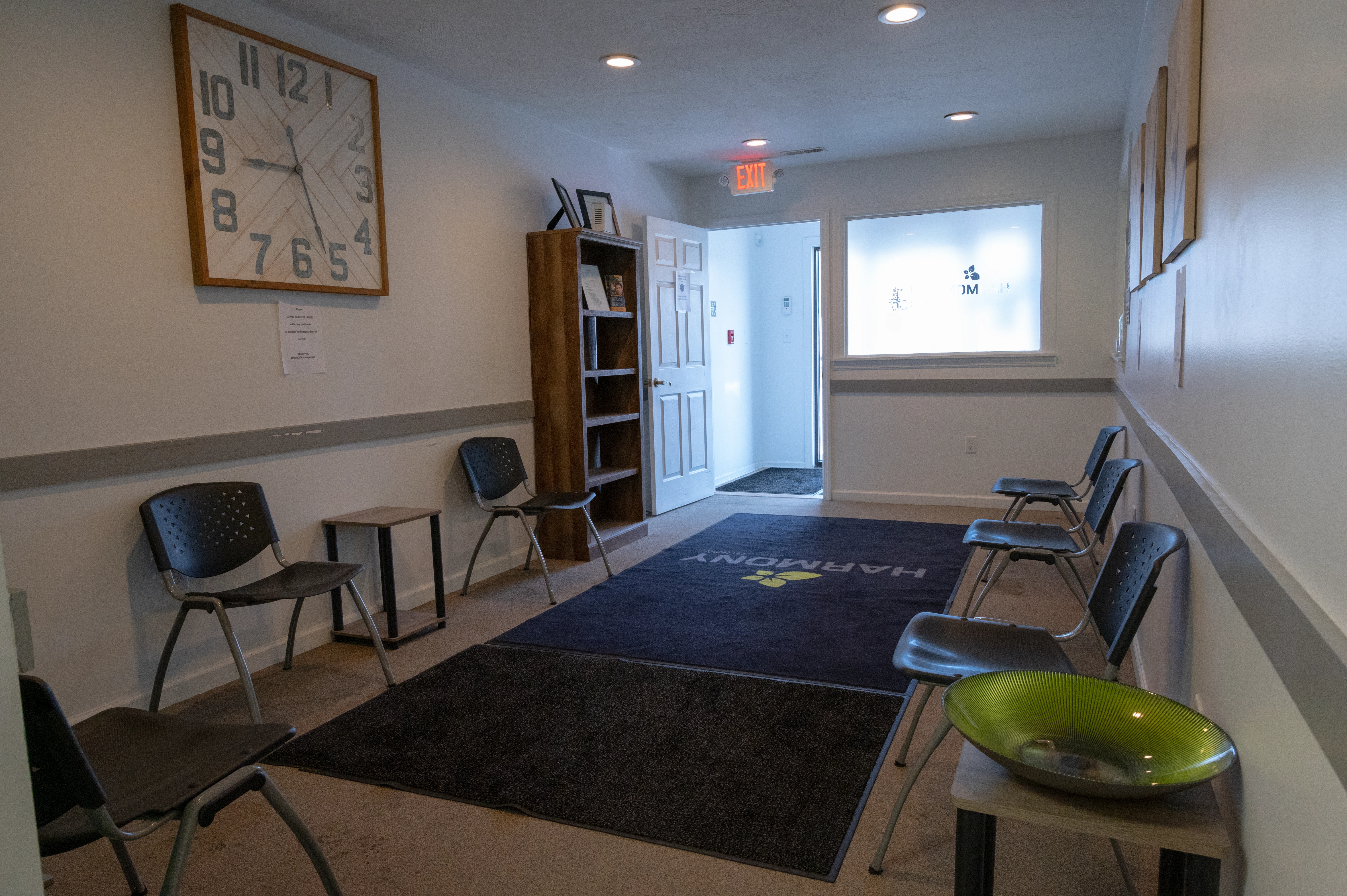 Clinic lobby with reception area, large wall clock, seating chairs, entrance doors, and exit sign