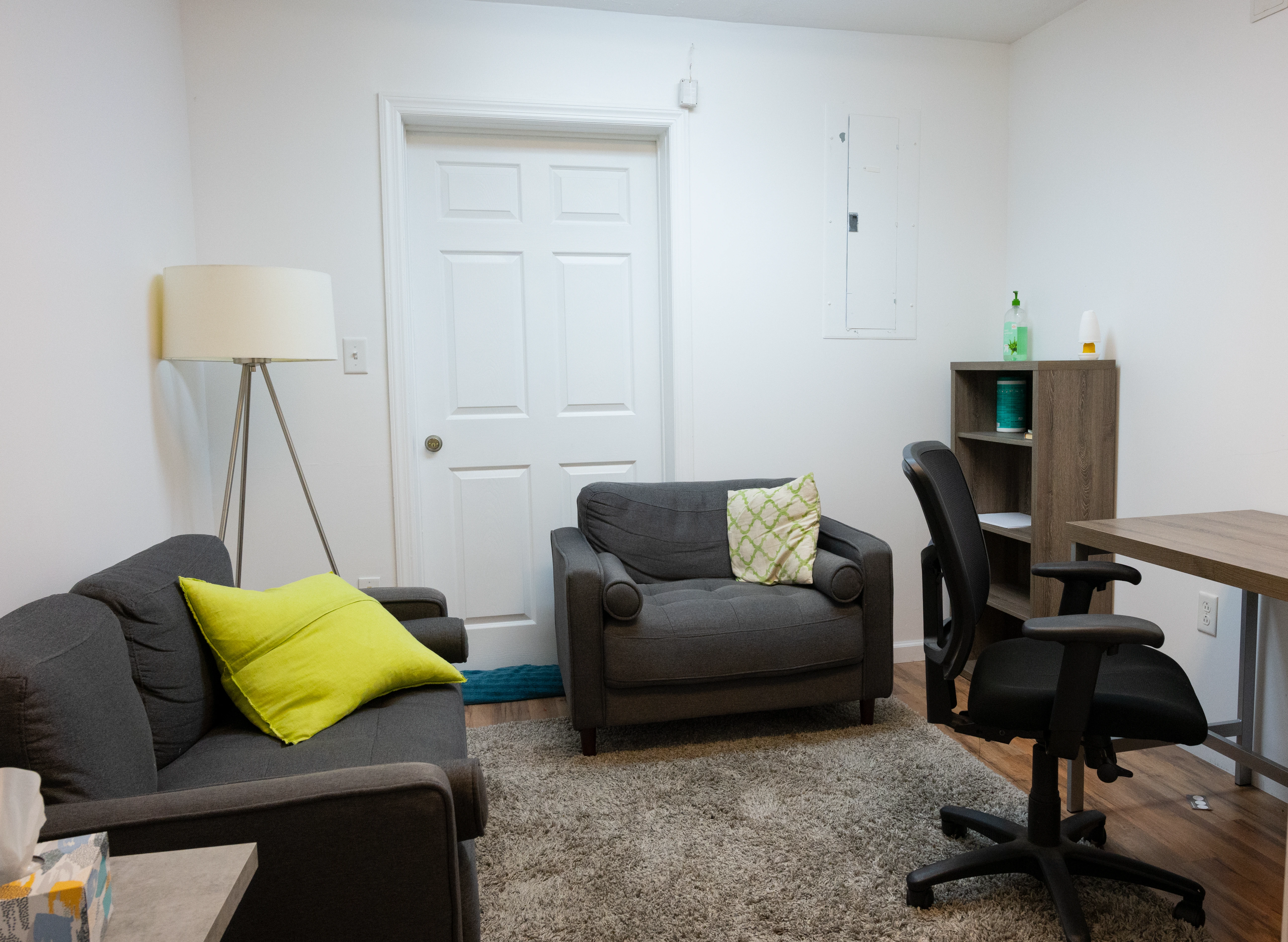 Waiting room with dark armchairs, floor lamp, wooden shelving, and desk with office chair