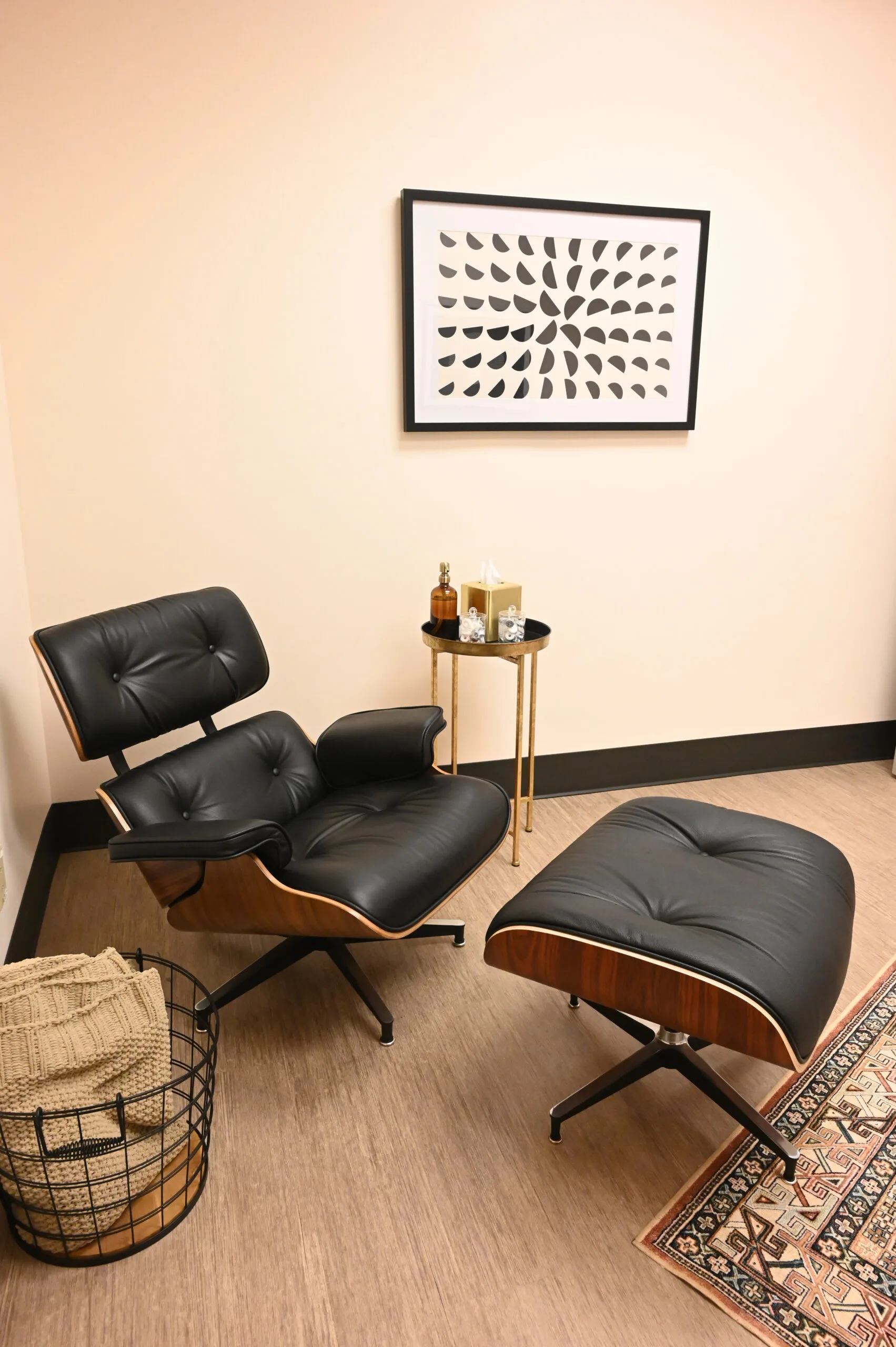 Lounge seating area with black leather chair, ottoman, side table with bottles, and geometric wall art