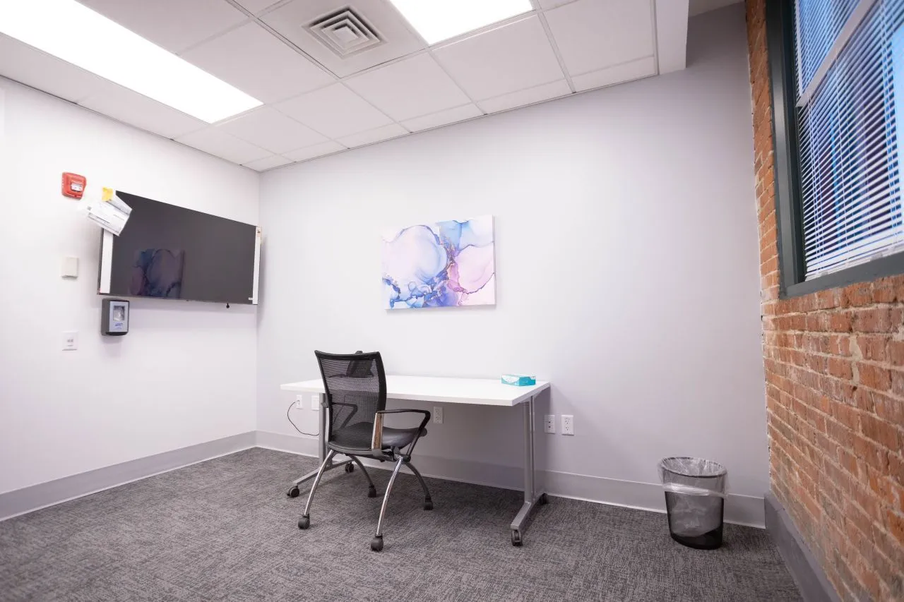 Consultation room with desk, black mesh chair, wall-mounted TV, and abstract blue artwork