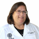 Caroline Olenski, APRN wearing white coat with stethoscope, smiling at camera