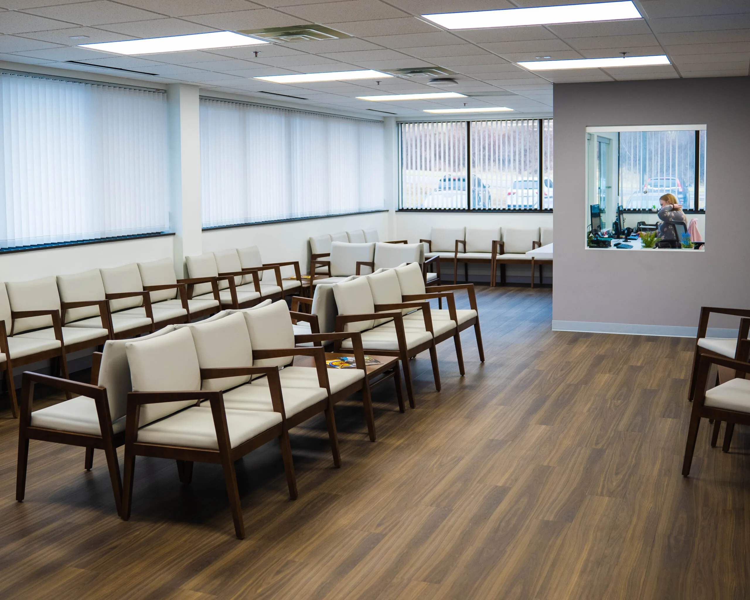 Spacious waiting area with multiple cushioned seating arranged in rows, bright lighting, and windows with sheer blinds