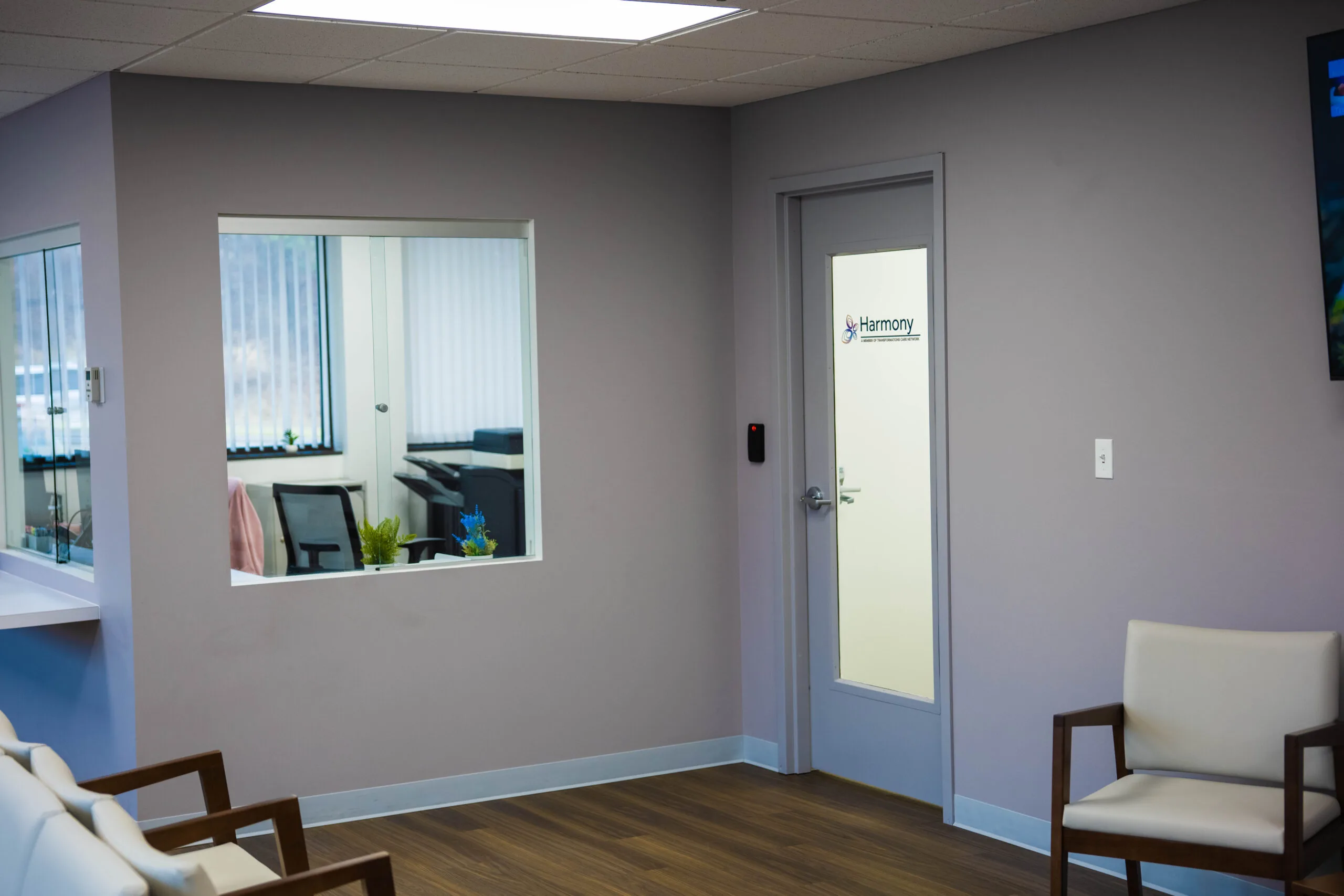 Harmony clinic waiting room with comfortable chairs, large window into office space, and branded door
