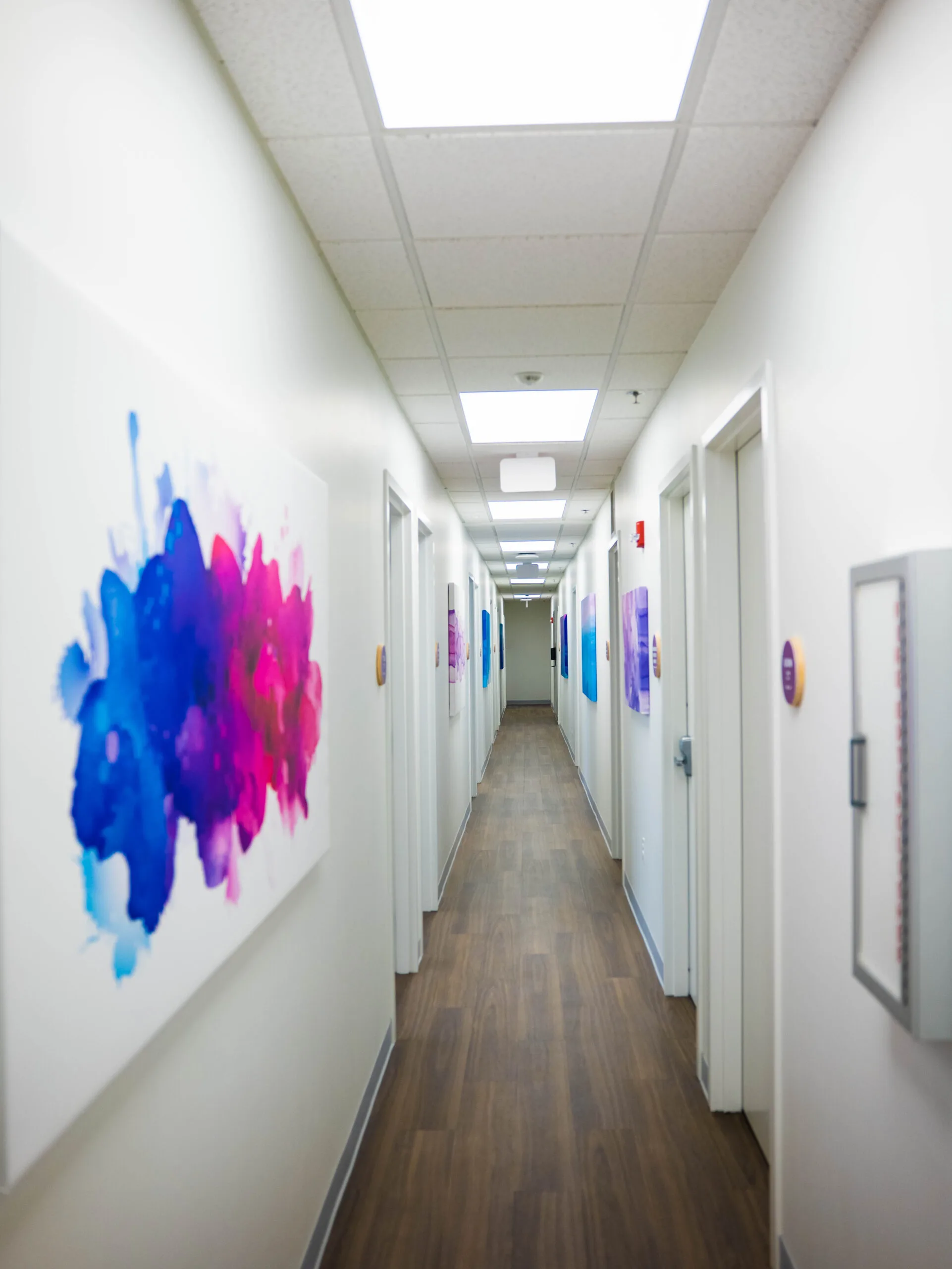 Hallway with colorful abstract artwork on walls and treatment room doors at Harmony clinic