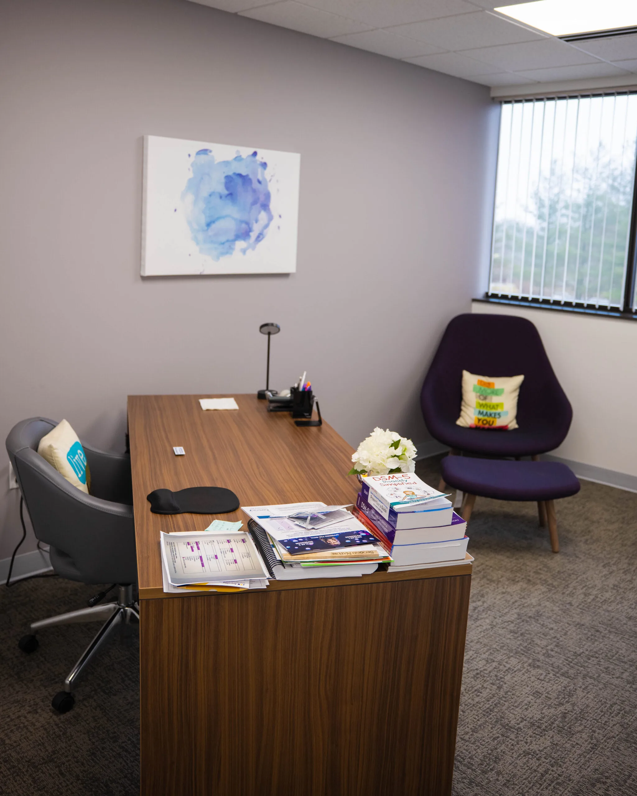 Office consultation room with wood desk, chairs, blue abstract artwork, and window