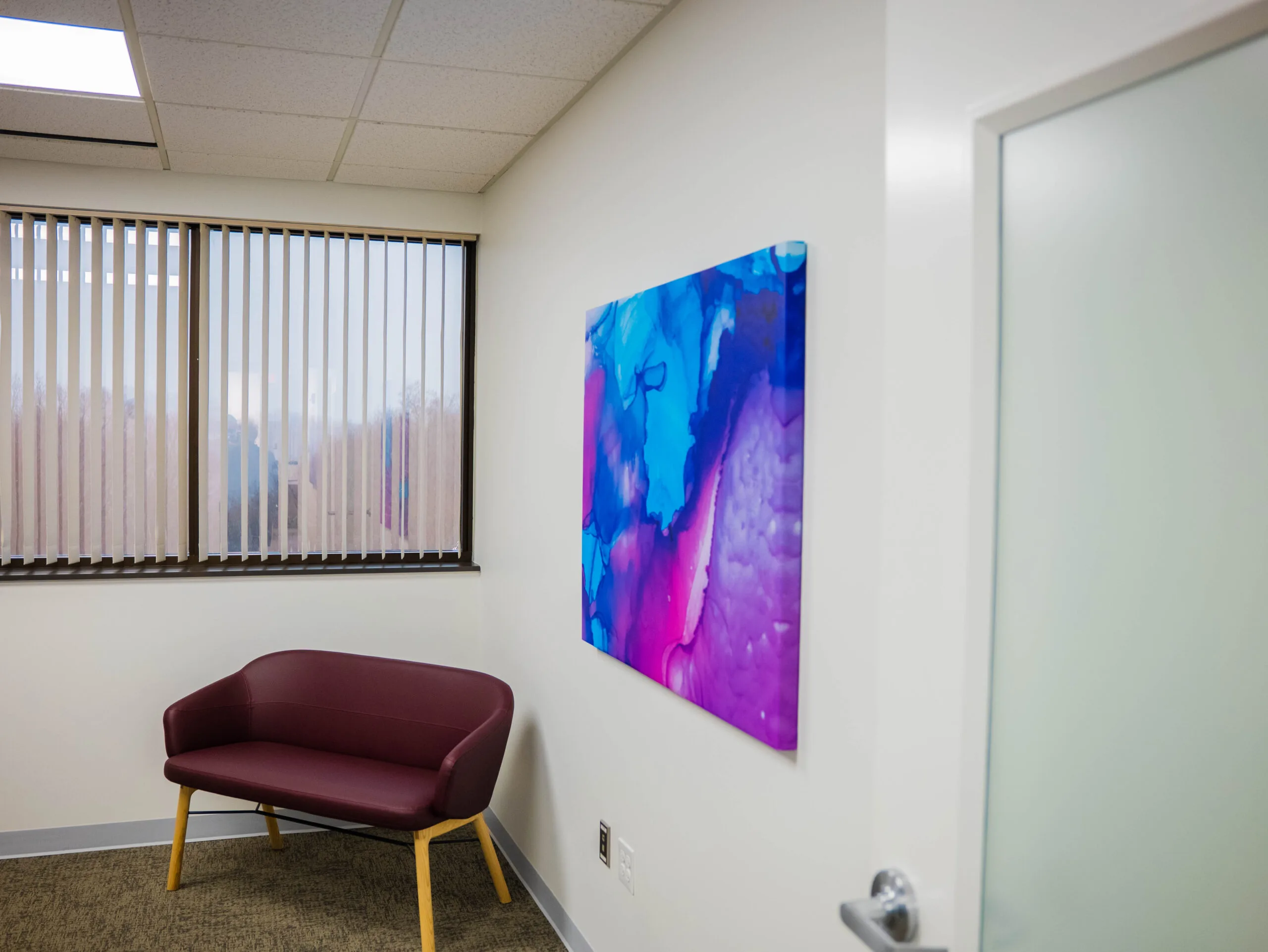 Waiting area with burgundy accent chair and abstract blue-purple artwork on wall