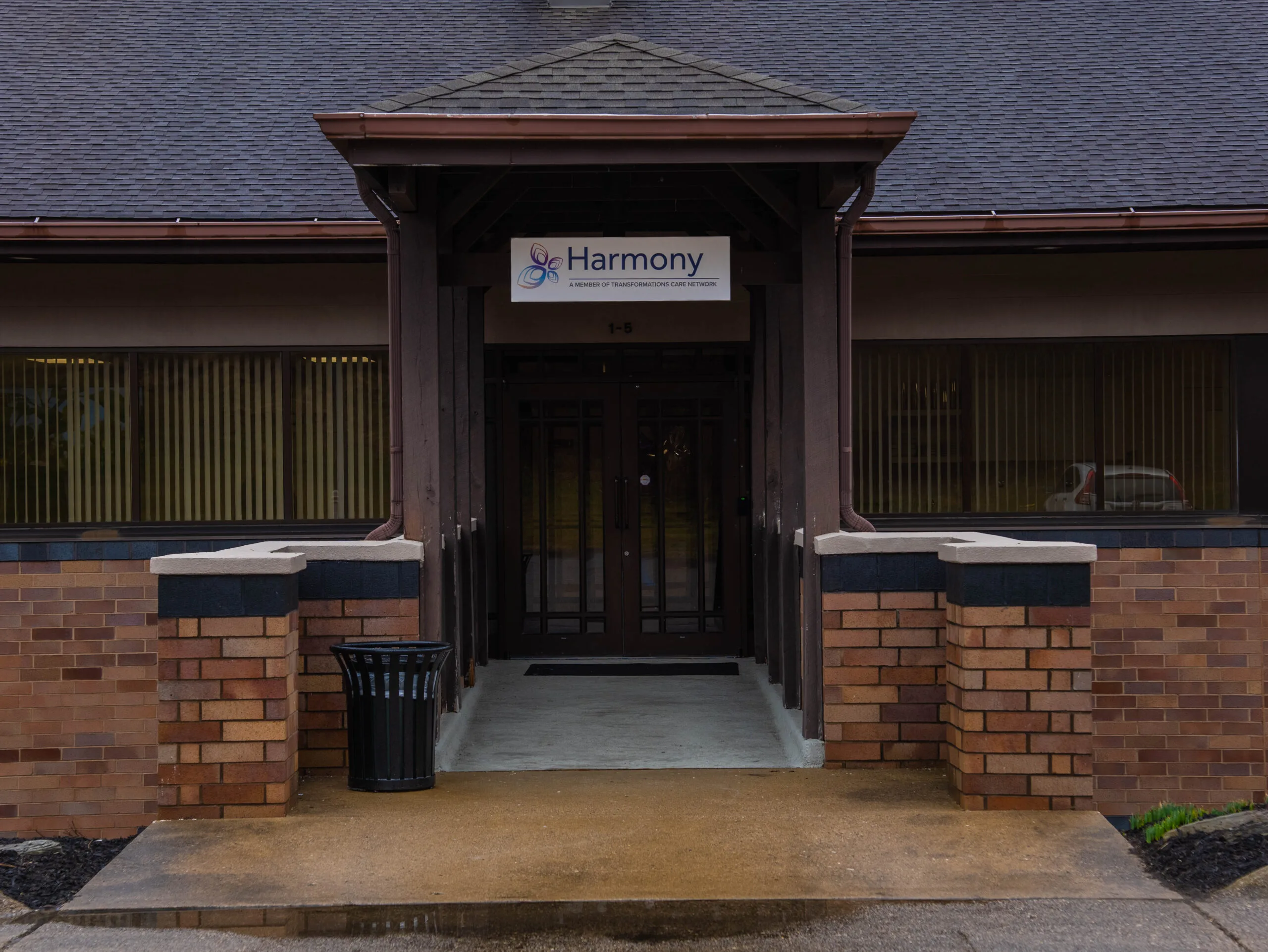 Harmony logo and signage above entrance doors of brick medical practice building with dark awning