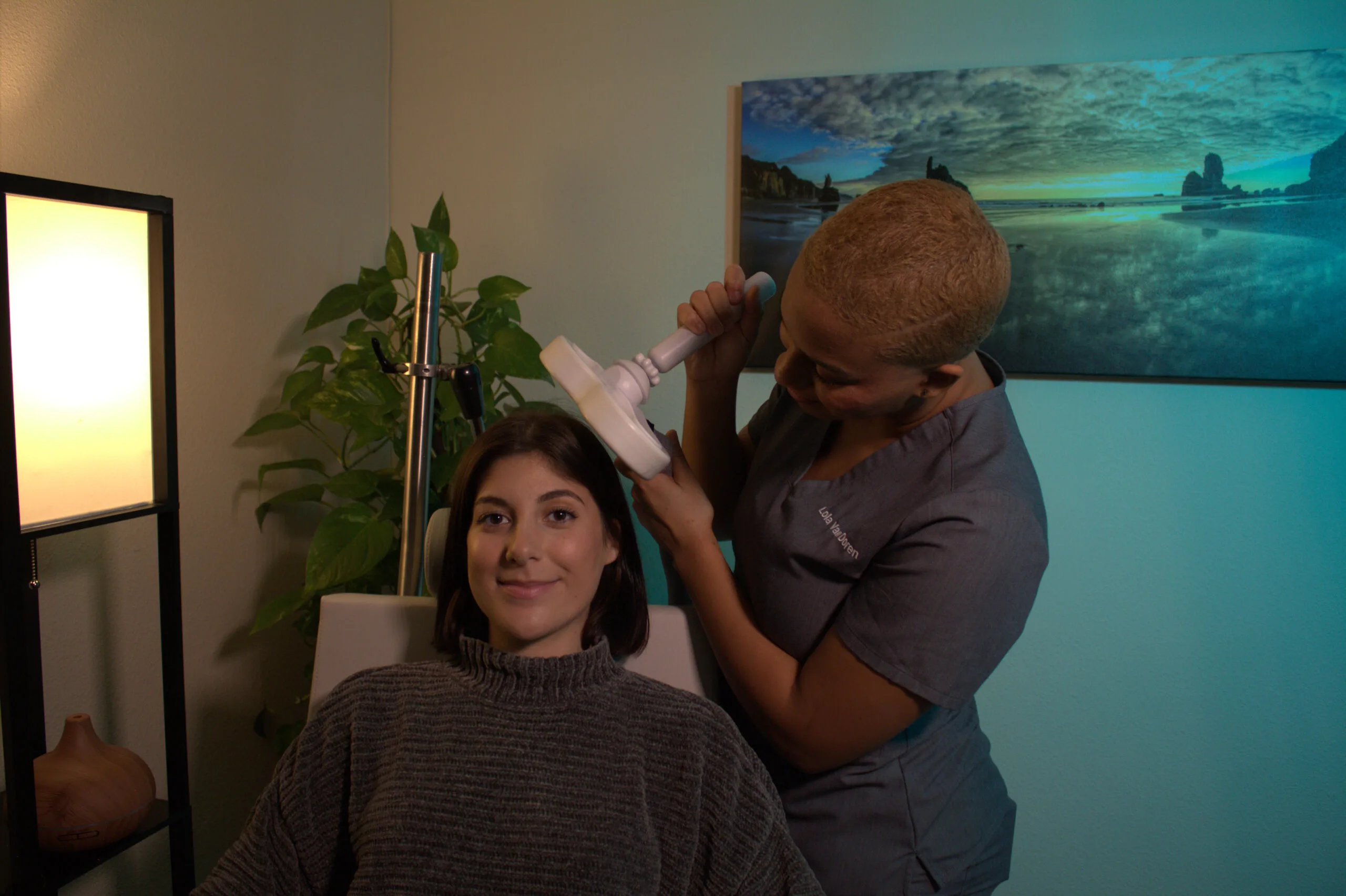 TMS therapist positioning magnetic coil on seated patient's head during treatment session