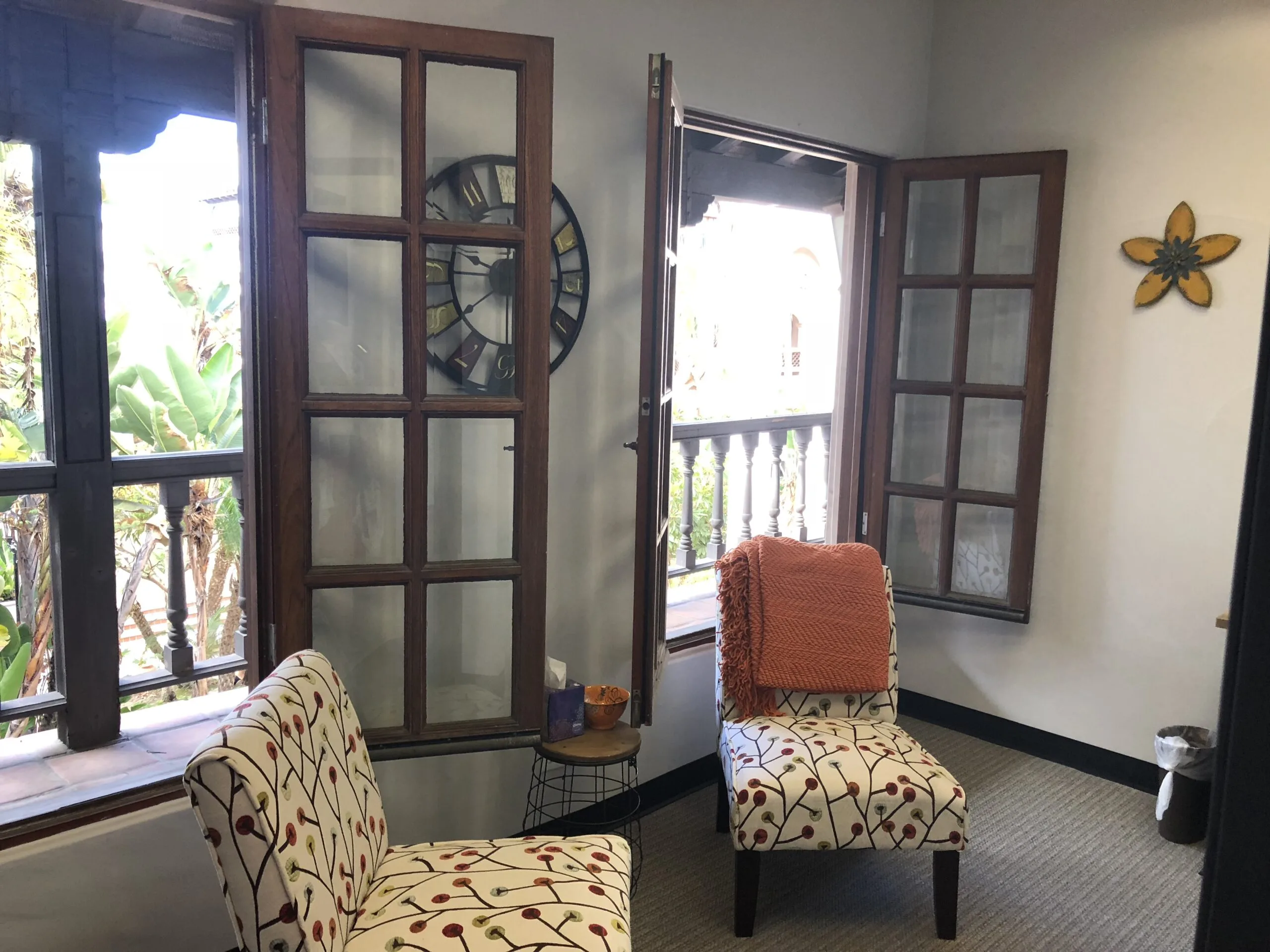 Costa Mesa office space with patterned armchairs, glass doors opening to outdoor balcony, and decorative wall clock