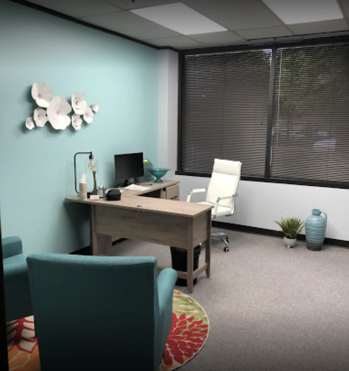 Executive office with light wood desk, white chair, turquoise accent wall, decorative white discs, and windows with black blinds