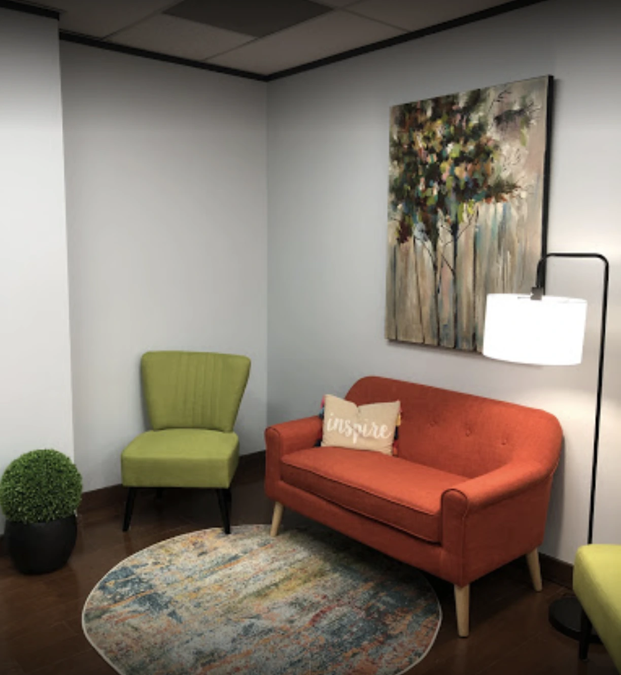 Therapy room with red sofa, lime green accent chair, round rug, landscape artwork, and floor lamp