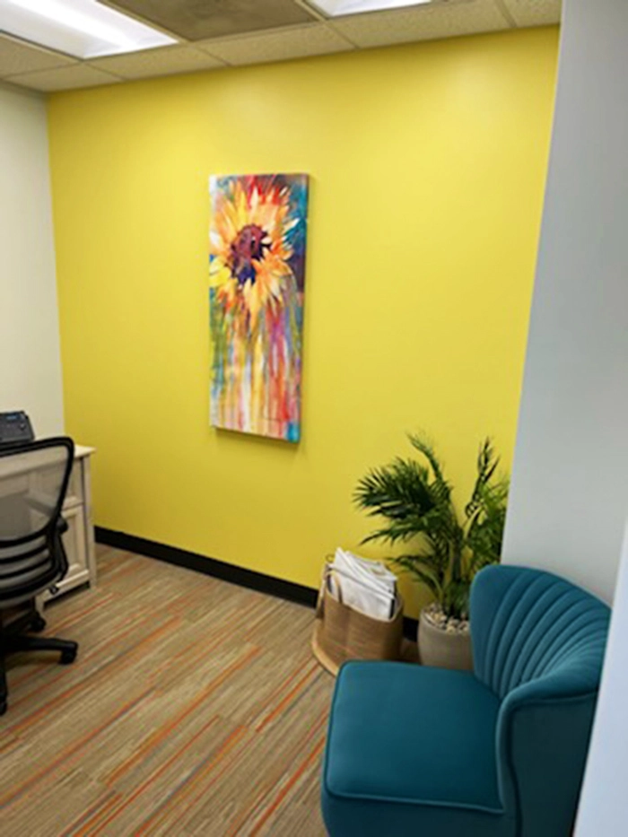 Grapevine office with bright yellow wall, colorful sunflower painting, teal chair, and green plants