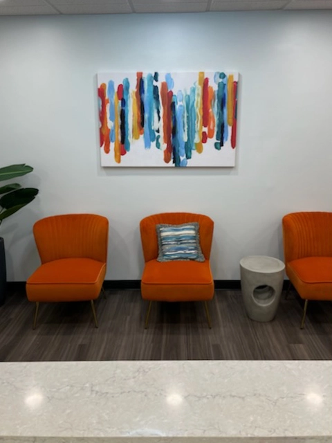 Grapevine waiting area with three orange chairs below abstract colorful artwork on white wall