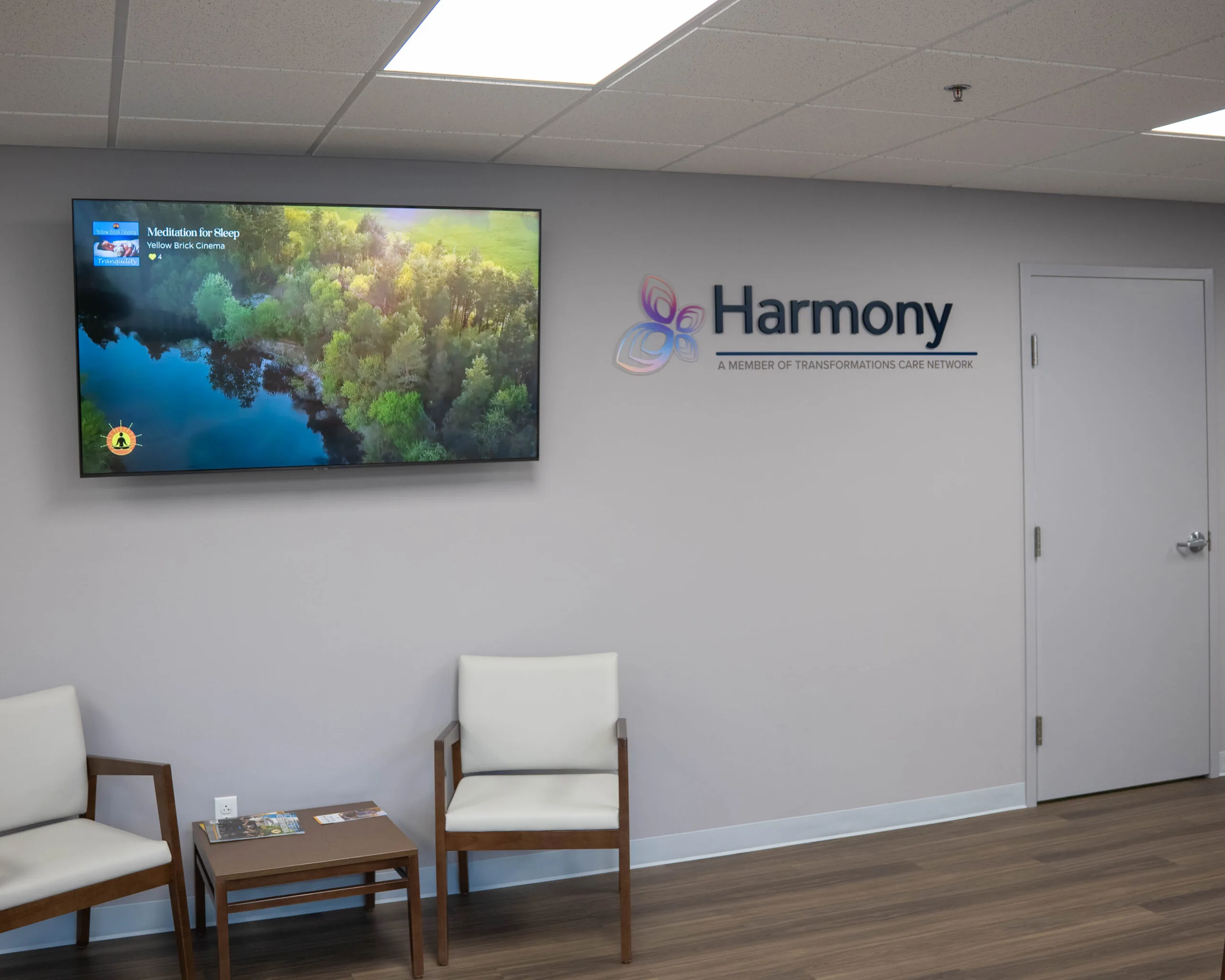 Harmony logo on wall above waiting area with mounted TV displaying nature scenery and cream chairs