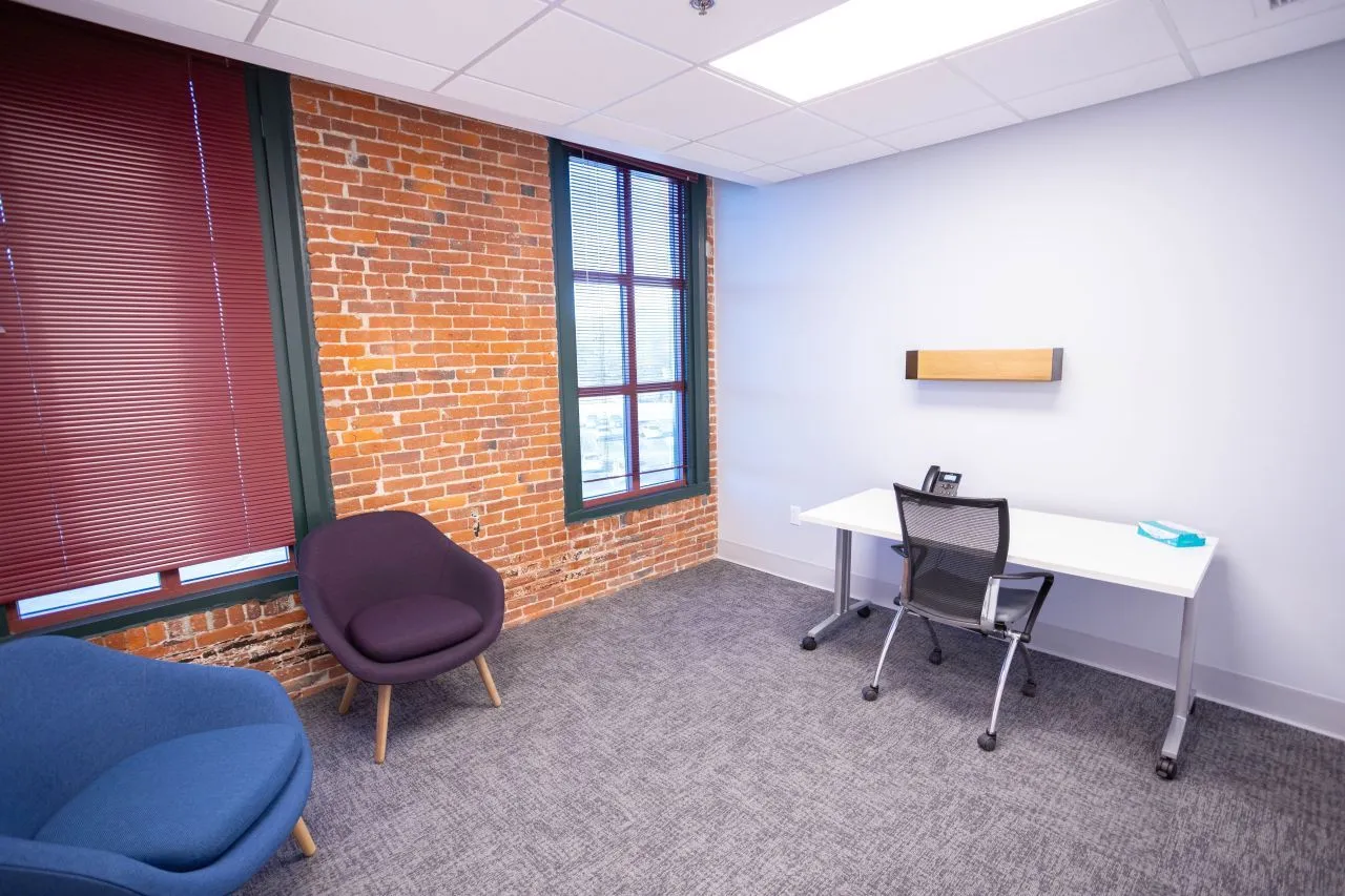 Office space with exposed brick wall, purple accent chair, blue seating, and desk with chair