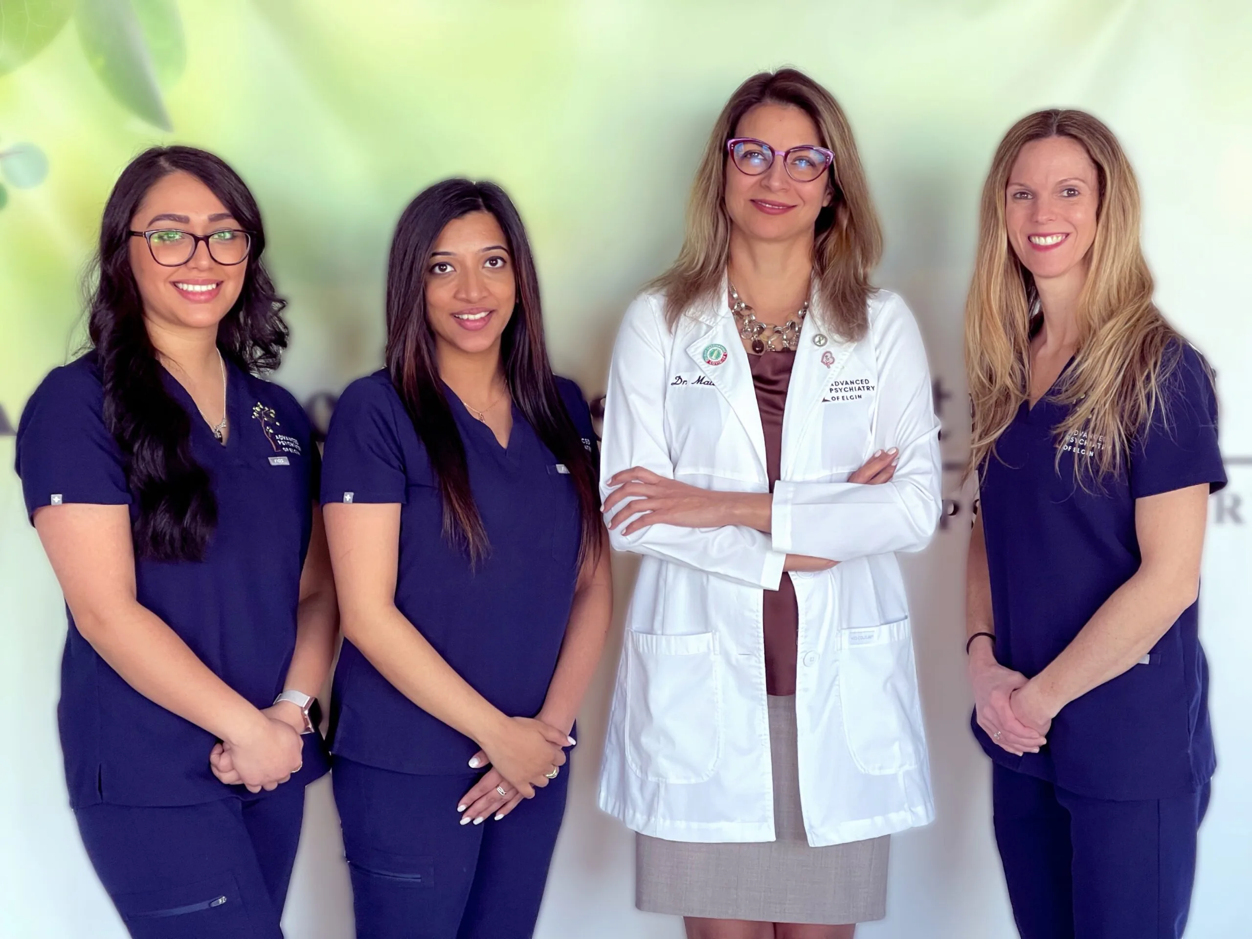 Four staff members posed together, three in navy scrubs and one in white coat with Advanced Psychiatry of Elgin branding