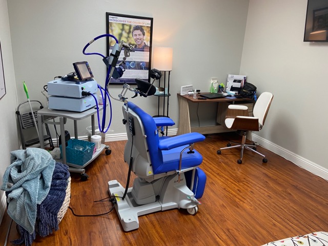 TMS therapy treatment room with blue medical chair, monitoring equipment, and mounted display screen