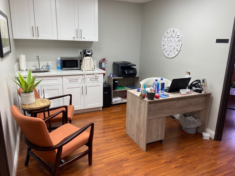 Office workspace with white cabinetry, potted plant, orange chairs, wooden desk, and printer
