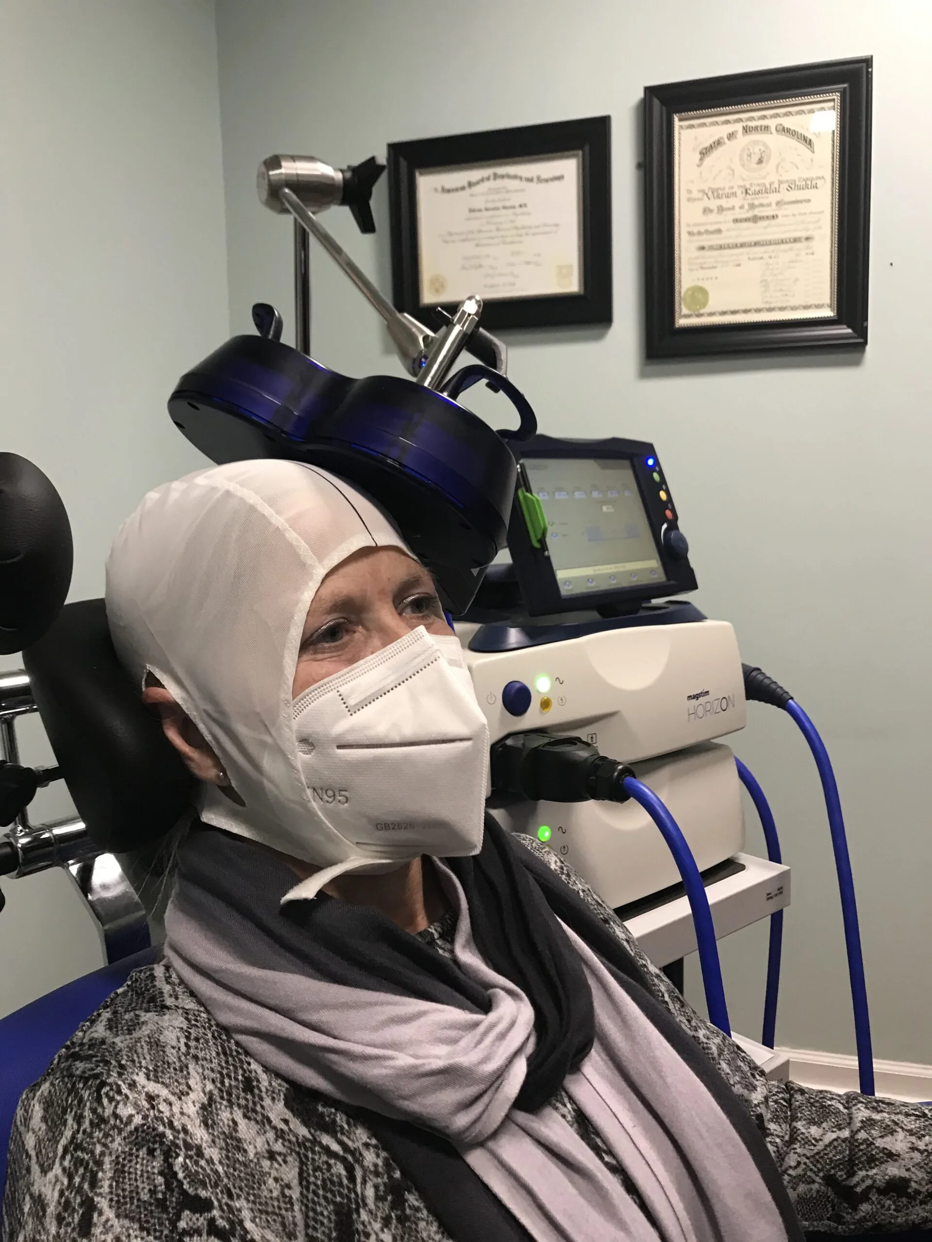 Patient receiving TMS treatment with coil positioned on head while wearing protective equipment