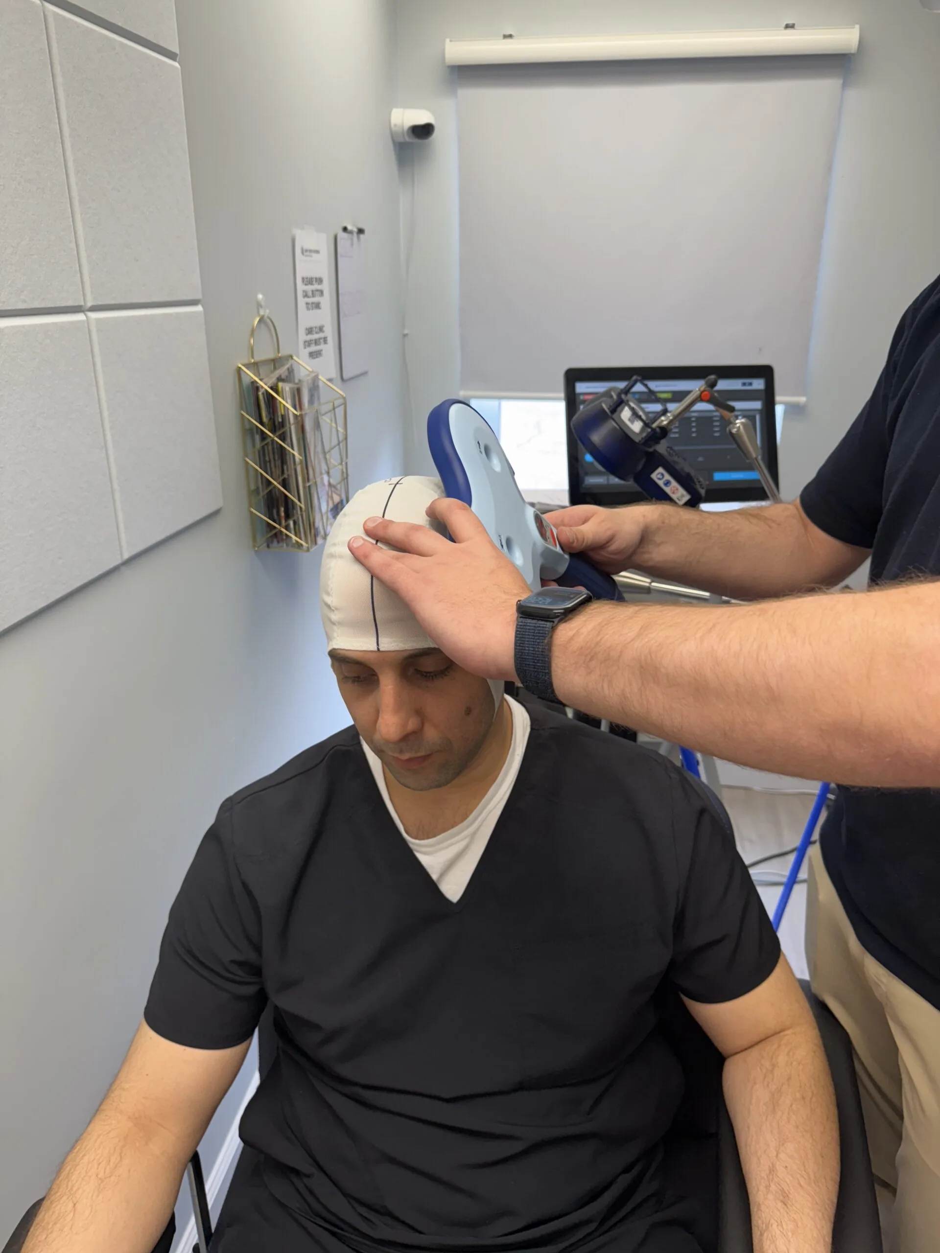 Practitioner positioning TMS coil on patient's head during treatment session in clinical room