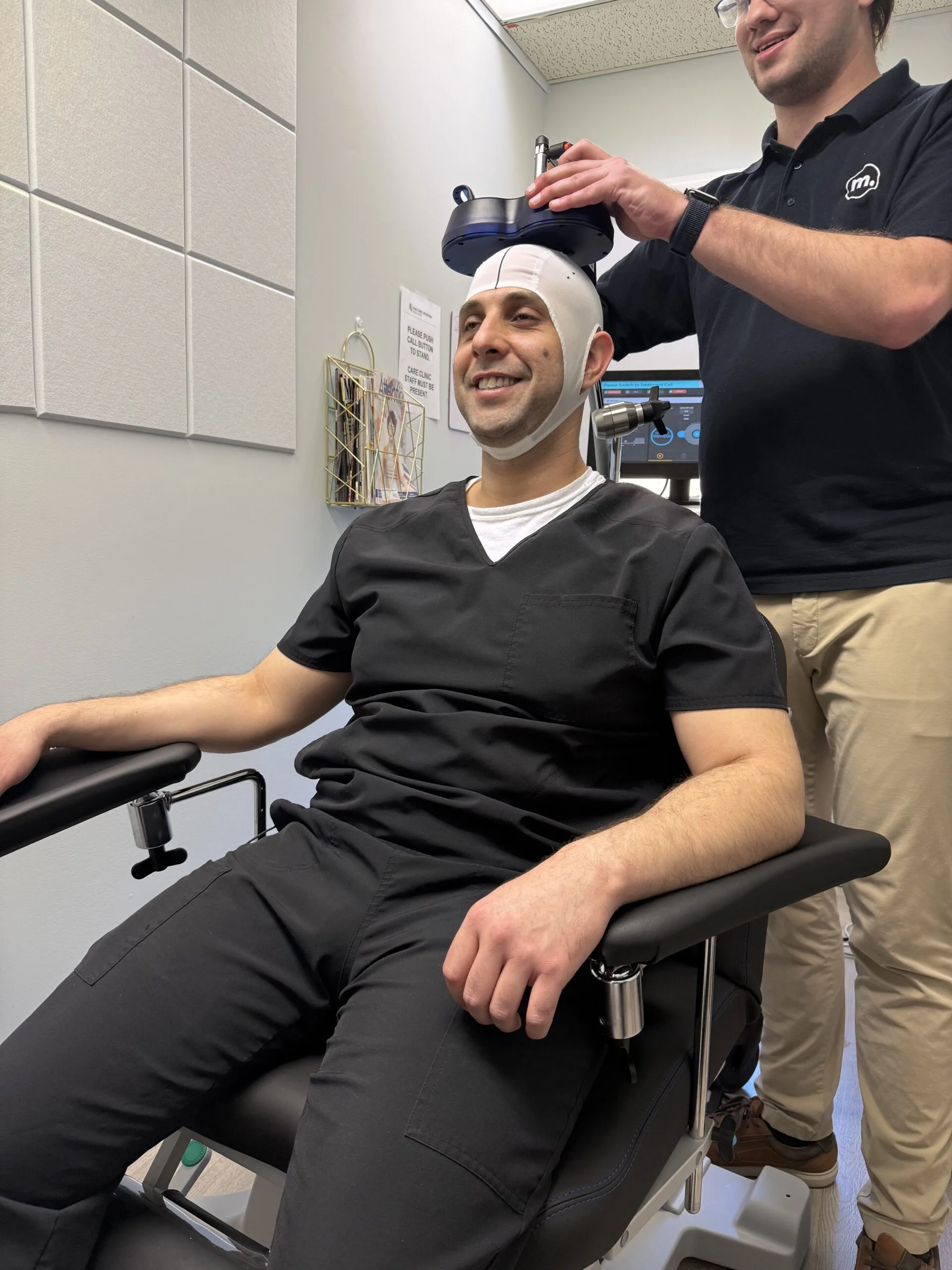 Technician fitting TMS coil cap on smiling patient's head in clinical setting