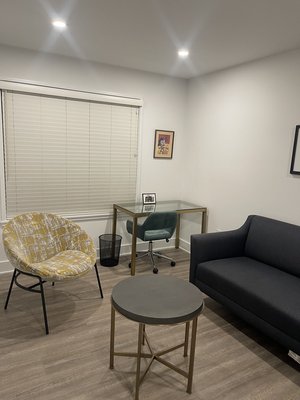 Private office space with black sofa, patterned armchair, round side table, and desk with computer