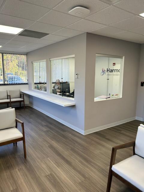 Reception area with white counter desk, waiting chairs, and view into treatment room with Harmony signage