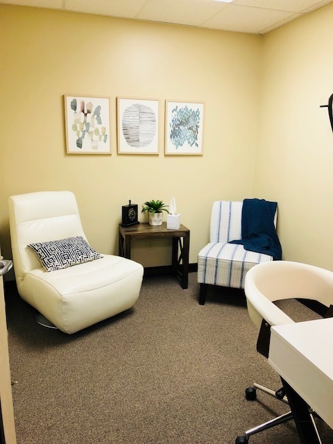 Comfortable waiting room with yellow walls, white accent chair, striped blue and white chair, small dark table with plant, and framed artwork