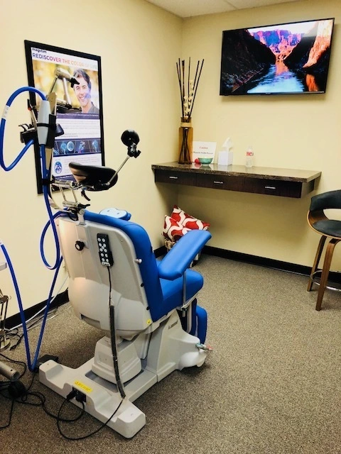 TMS treatment chair with blue padding and overhead coil apparatus, monitor displaying nature scene
