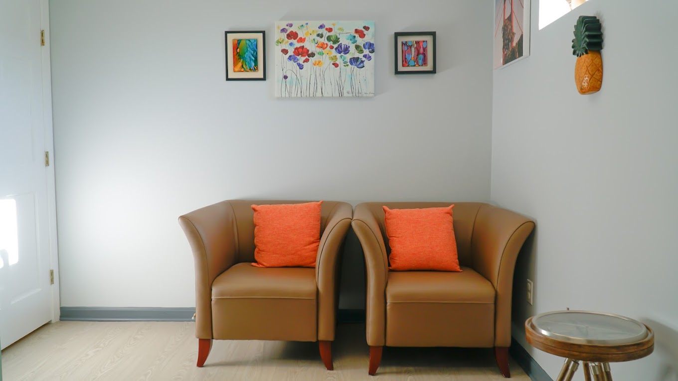 Office waiting area with tan leather armchairs with orange pillows, colorful wall art, and wooden side table