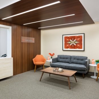 Modern therapy office waiting area with wood ceiling, orange accent chair, and gray sofa