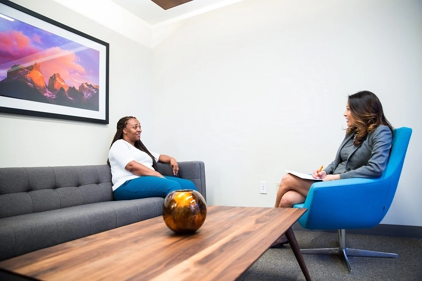 Therapist taking notes during consultation with patient seated on gray sofa in office setting